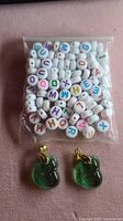 White alphabet letter beads in a sealed plastic bag alongside two green translucent fox-shaped resin pendants with gold-tone bails.