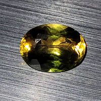 Large oval faceted bi-colour tourmaline gemstone showing yellow and green colors on a dark textured surface.