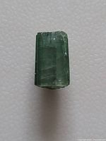 Rectangular green tourmaline gemstone against a white background showing natural inclusions and polished surface.