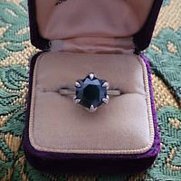 Lab created black diamond solitaire ring displayed in a closed Violet velvet ring box with beige interior lining.