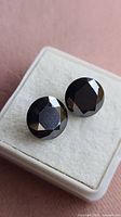 Two round faceted black stones on a white display stand, showing the larger and smaller diamond side by side with glossy faceted surfaces.