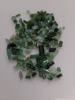 Varied collection of blue-green tourmaline gemstones in various sizes and shades on a white background.