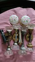 Overview of eight crystal/glass door knobs and two white porcelain door knobs with floral pattern, plus brass hardware laid out on fabric.