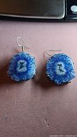 Pair of large blue geode earrings with visible crystalline texture and sterling silver hooks lying flat on a surface.