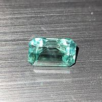 Close-up top view of the bright green sapphire showing the cut and clarity on a dark textured background.