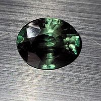 Close-up of large oval green tourmaline with faceted cuts, showing depth of color and reflection on a wooden surface.