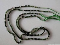 Two strands of green tourmaline faceted beads laid out in a loose coil to show bead size and color variation.