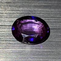 Close-up of the oval faceted purple-blue iolite gemstone showing clarity and facets under bright light.