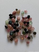 Top view image of a collection of mixed smooth and faceted natural tourmaline beads of different colors and sizes.