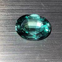 Close-up image showing the oval cut and facets of the lab-created blue-green tourmaline on a textured dark surface.