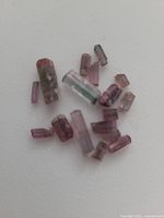 Close-up photo of multiple small raw bi-colour tourmaline crystals on white background, showing pink and purple tones.