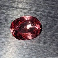 Close-up photo of oval cut purplish-pink rubellite tourmaline showing multiple facets and reflections under bright light.