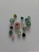 Top-down photo showing 14 small tourmaline slices of various colors on a white background.