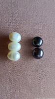 Five pearls laid out on fabric, showing three white Freshwater pearls and two dark South Sea pearls, all button-shaped and undrilled.