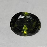 Close-up photo of the oval cut sphene gemstone showing dark green color and light reflections.