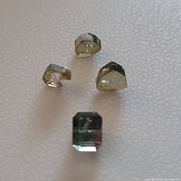 Four watermelon tourmalines comprising one faceted gem and three mineral slices arranged on a textured light background.
