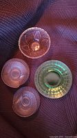 Top-down view showing three pink Depression glass dessert dishes with waffle pattern and one green glass plate all on textured fabric.