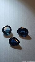 Three blue sapphires with different cuts (oval, round, pear) under lighting showing color and facets.