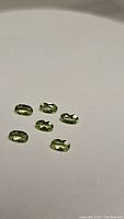 Six oval cut apple green peridot gemstones arranged on a white background, showing their color, size, and clarity.