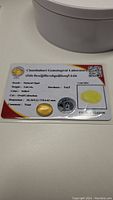 Photo of the certified yellow opal gemstone card showing certification details including weight 3.64 ct, color yellow, cut oval cabochon, dimensions 10.84 x 12.73 x 4.62 mm.