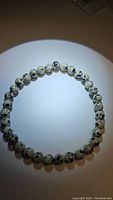 Top view of natural dalmatian jasper bracelet formed in a circle on white background showing black spots on light colored beads.
