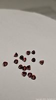 Top-down close-up photo showing 15 small bullet-shaped garnet gemstones spread on a white background, highlighting their deep red color and clarity.