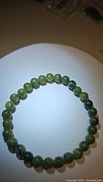 Photo showing full view of green jade bracelet laid flat in circle, lighting highlights polished surface and natural green coloring of beads.