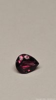 Pear cut natural sapphire with hot pink and purple coloration on a neutral background, showing facets and clarity.