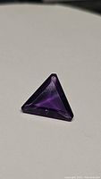 Close-up photo showing the deep purple trillion cut Brazilian amethyst gemstone from a side angle, highlighting the gemstone's clarity and sharp facets.