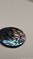 Oval-shaped natural abalone cabochon doublet with vivid iridescent patterns and colors, photographed on light background to highlight reflective surfaces.