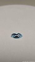 Close-up image of a marquis cut sky blue topaz gemstone lying flat on a white surface showing facets and clarity.