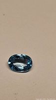 Close-up photo of an oval cut lagoon blue zircon gemstone on a light background, showing cut facets and clarity.