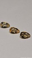 Three pear cut golden citrine gemstones laid out side by side on a flat surface, showing clarity and faceting.