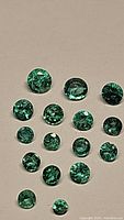 15 round emeralds arranged in rows on a beige background showing size variation from largest top row to smallest bottom stone