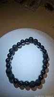 Top view of natural lava stone and hematite bead bracelet on a white surface showing bead texture and layout.