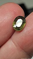Close-up photo of oval cut yellow-green sapphire held between fingers showing cut facet and color variation.
