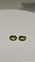 Clear image of both oval cut apple green peridot gemstones placed side by side showing their color, cut, and size.