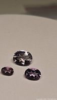Three natural pink amethyst gemstones of varying sizes with oval cuts, placed on a white surface showing their clarity and color.