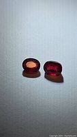 Photo showing two deep red oval cut natural rubies on white background, highlighting their color and inclusions.