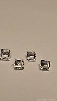 Four square cut natural white topaz gemstones displayed on a plain background, showing size and clarity.