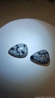 Pair of polished snowflake obsidian cabochons with distinctive white patterns on a black base, lit to highlight surface texture and pattern.
