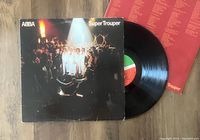 Photo of ABBA Super Trouper vinyl record partially outside its album cover, showing the front cover artwork and a red inner sleeve with track listings.