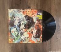 Colorful illustrated album cover with band members' portraits and the vinyl record partially pulled out.