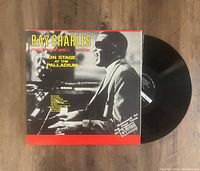 Black vinyl record partially out of album cover, cover showing Ray Charles playing piano in black and white photo with yellow and red text.