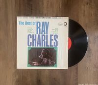 Vinyl LP of The Best of Ray Charles partially outside the album cover on a wooden floor.
