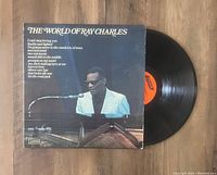Vinyl record partially removed from album cover showing the album cover with photo of Ray Charles and song titles, and the black vinyl disc with orange label.