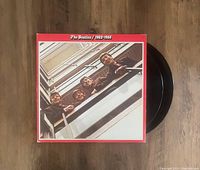 Front of the vinyl record cover showing The Beatles looking down from a balcony with red border and title at top, two black vinyl records partially visible.