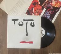 Vinyl record partially in cover with Toto logo visible on label and cover, along with inserts spread out showing images and lyrics.