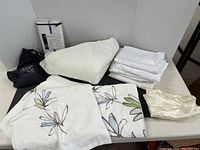 Photo showing white flannel sheet, folded plain white pillow cases, floral patterned duvet cover and pillow cases, cream-colored satin-like pillow case, and a black bag.