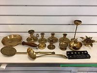 Front view showing full lot of brass items including candle holders, brass pan, kitchen utensils, and a decorative piece.